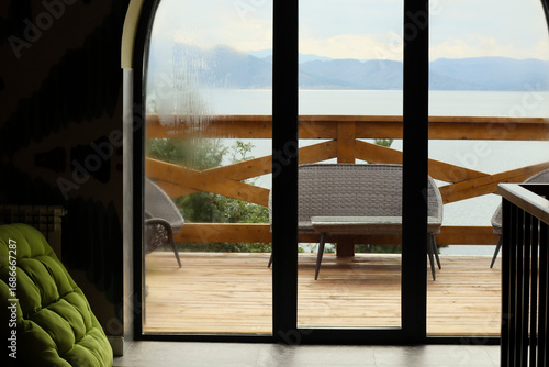 Scenic view of Bukhtarma Reservoir and mountains from the window of a resort hotel with wicker chairs, peaceful early autumn atmosphere.