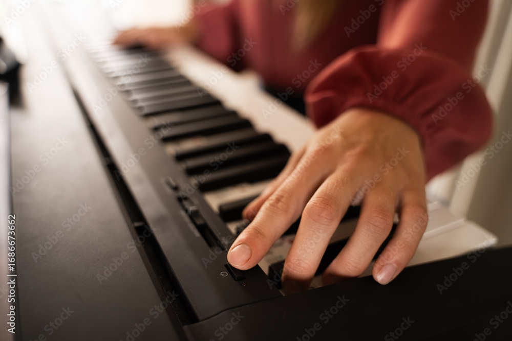 Fototapeta premium Close-up of Caucasian woman's hand turning on an electric piano before starting musician lesson indoors with cozy warm light, selective focus