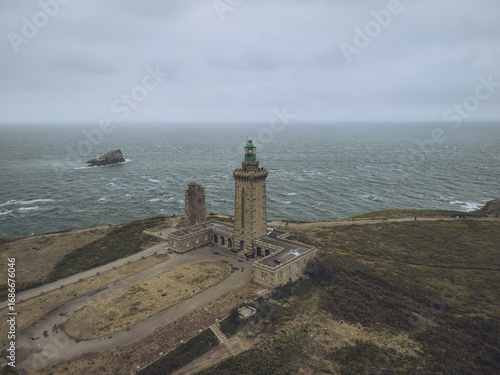 Aerial view of the majestic Cap FrÃ©hel lighthouse standing tall against the turbulent sea, with the rugged coastline adding drama to the scene, PlÃ©venon, Bretagne, France.