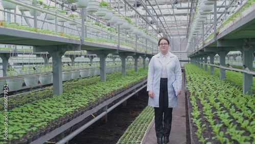 Photos Smiling woman ecologist walking through greenhouse, inspecting plant growth