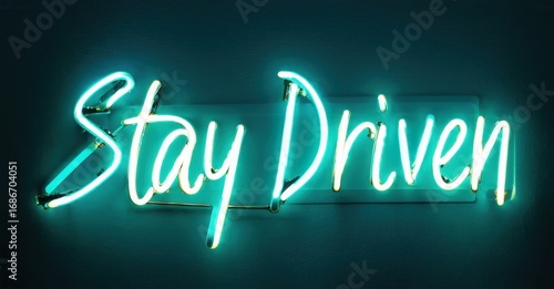 Bright neon sign displays Stay Driven. Turquoise glow contrasts dark background. Simple typography, motivational message, modern aesthetic.