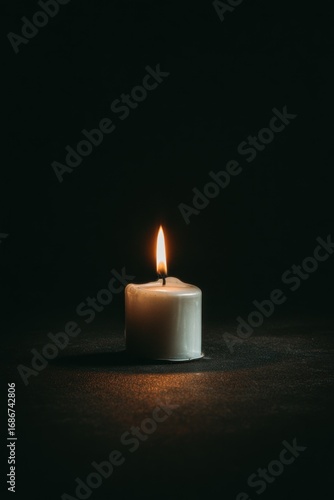 A glowing white candle rests on a dark surface, the warm flame flickering against the inky backdrop, creating a serene and intimate ambiance