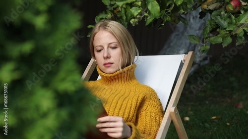 woman reading book in garden near apple tree in autumn