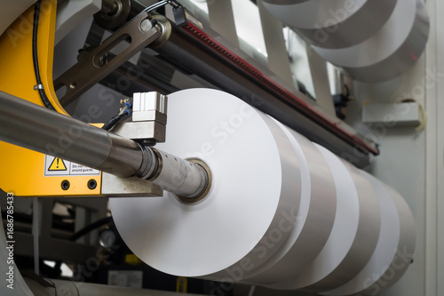 The process of winding paper self-adhesive tape into rollers of printing offer paper for printing houses. Close-up of the paper cutting and rewinding machine. Selective focus