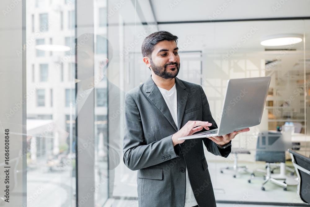 Fototapeta premium A business professional is actively engaged in their work on a laptop while seated in a contemporary office setting, surrounded by modern decor and technology