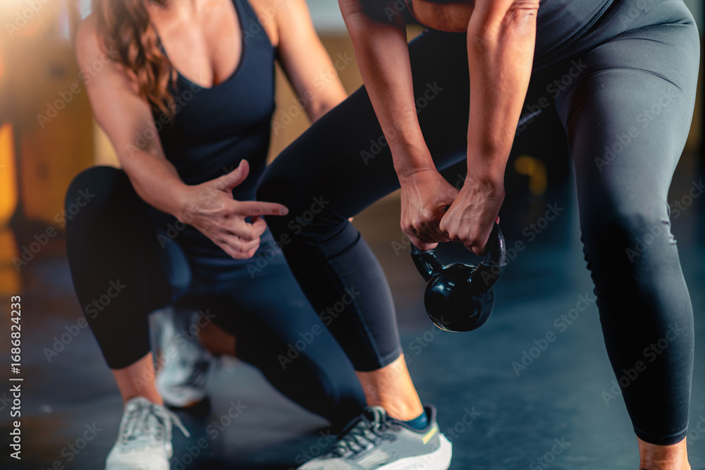Fototapeta premium Using a kettle bell with a personal trainer, a mid adult woman improves power and flexibility in the gym. Customized workouts support health goals and enhance overall wellbeing.