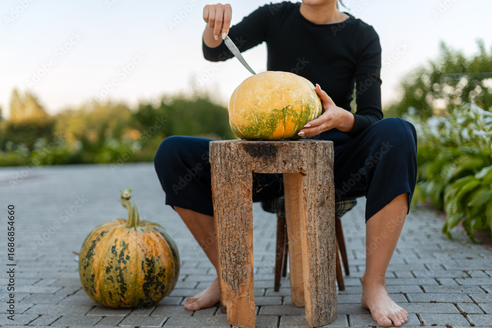 Fototapeta premium Woman carving pumpkin sitting on wooden stool in the garden