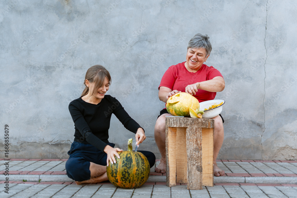 Fototapeta premium Two women carving pumpkins for Halloween party decoration are having fun