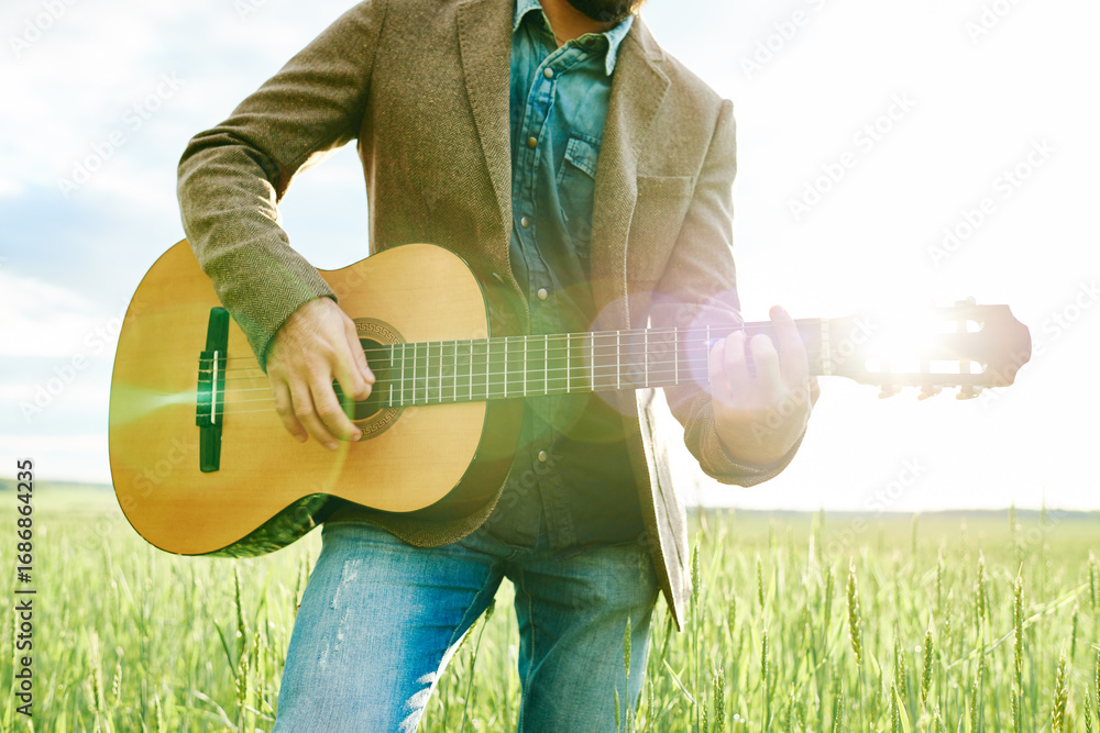 Φωτογραφία Caucasian young adult man playing acoustic guitar outdoors in field, strumming i