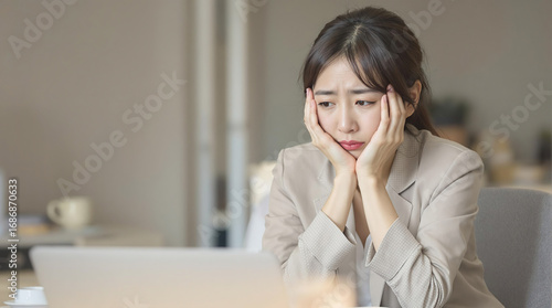 オフィスで頬に手を当てて悩むアジア人の女性会社員