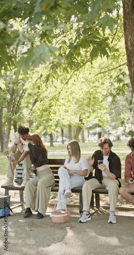 A group of young friends are hanging out together in a vibrant park, each engrossed in their mobile phones. This scene captures modern social interaction and digital connectivity outdoors.
