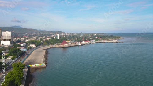 A beautiful aerial view of the capital city of Dili, Timor-Leste. The coastline, Dili Port, and the city blend with the calm blue sea on a sunny day.