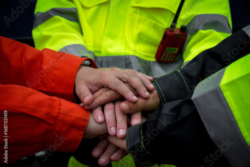 Teamwork and collaboration are essential in safety focused environments, as shown by hands of workers in bright safety gear coming together in unity