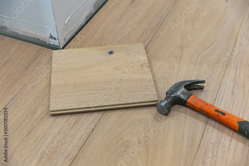 Single wooden plank with visible nail dent lying next to hammer on installed wood flooring during home renovation or repair process