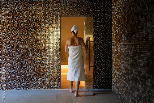 A woman enters a luxurious Turkish bath, bathed in a warm and relaxing atmosphere. The walls are covered with splendid mosaics that reflect the light. An oasis of well-being.