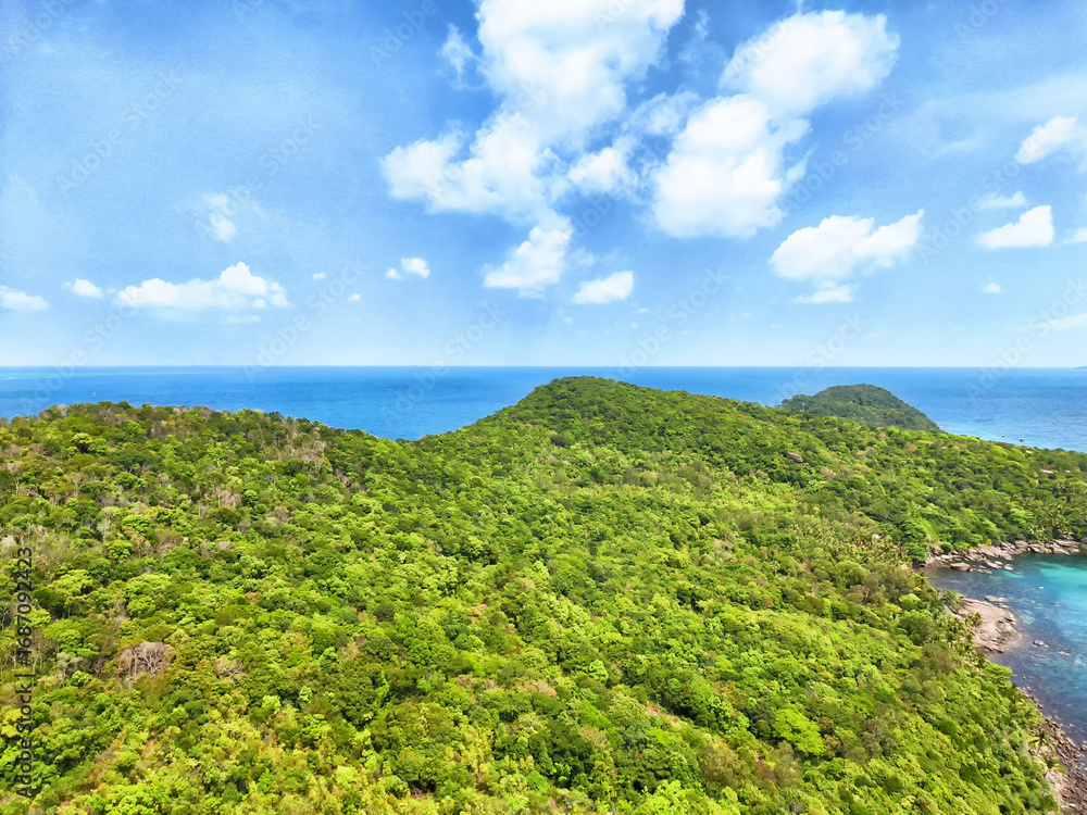 Fototapeta premium Lush green hills meet serene blue ocean under a vibrant sky at a tropical coastal location