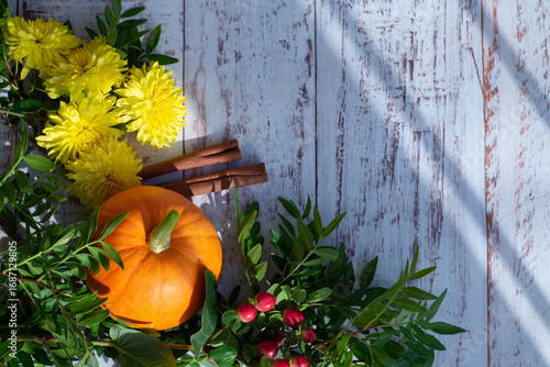 Autumn bright colored background for text, a composition of pumpkins, yellow flowers, and green branches on a wooden table