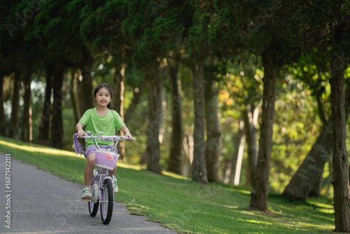 Wallpaper Mural Joyful young girl riding bicycle through scenic park pathway surrounded by lush trees and greenery during sunny day filled with happiness and adventure Torontodigital.ca