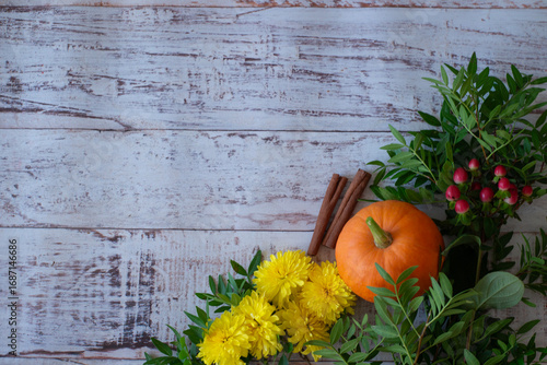 Autumn bright colored background for text, a composition of pumpkins, yellow flowers, and green branches on a wooden table
