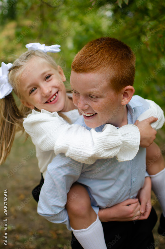 Fototapeta premium A little girl sits on the boy back and hugs him with her arms.