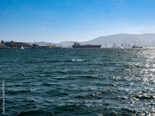 Cargo ships anchored up in the bay of Algeciras in front of Gibraltar and with Algeciras and the cranes in the Algeciras harbour in the background