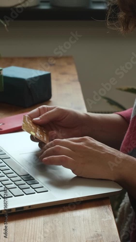 Vertical video. Woman shopping online for Christmas, sitting at desk, using payment card and laptop