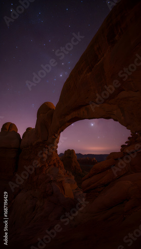Natural rock archway framing starry purple twilight sky and distant mountains night