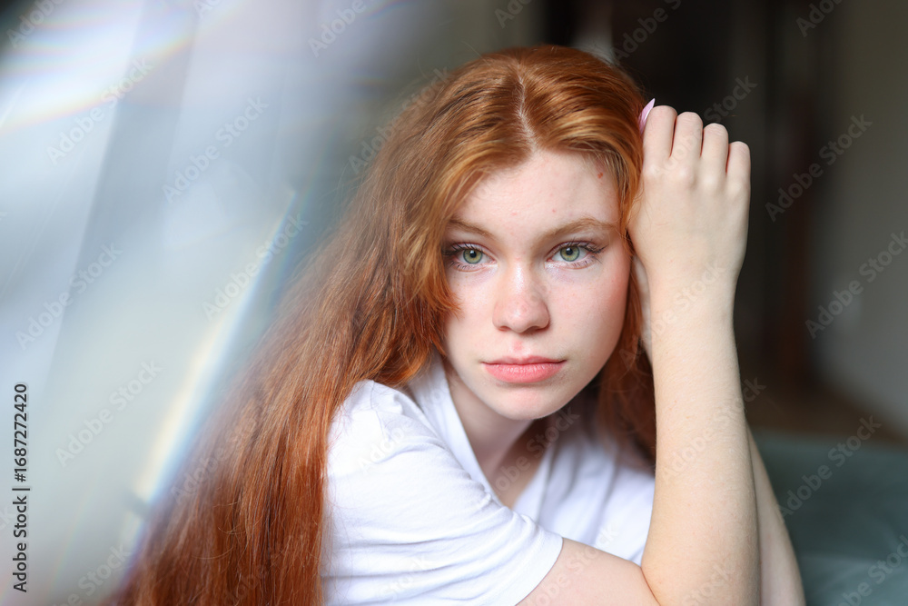 Fototapeta premium Portrait of a young girl with long red hair and green eyes in natural light, wearing a white t shirt.