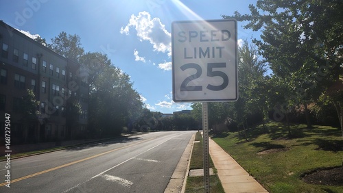 A 25 mph speed limit sign on a road between a park and an apartment building in the United States on a sunny day, American traffic rules and speed regulations, road signs on American urban highways