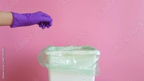 A hand in a protective glove throws a rag and crumpled paper into a trash can