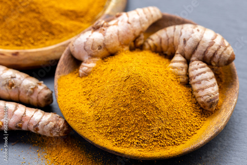 Fresh and ground turmeric root on a slate background