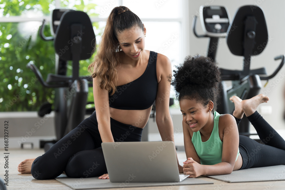 Fototapeta premium African American young girl and coach or personal trainer using laptop computer for training media online in fitness gym