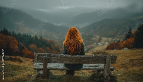 A person with fiery red hair sits alone on a rustic bench, gazing at a misty mountain scene with fall foliage