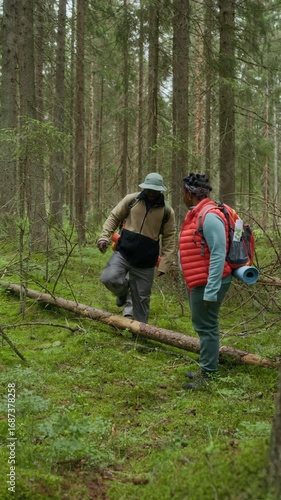 Wallpaper Mural Vertical full shot of active Black couple assisting their daughter to climb over fallen tree during forest hike, sharing adventure and family bonding Torontodigital.ca