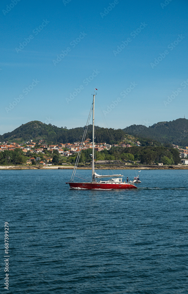 Fototapeta premium A sailboat in the estuaries of Galicia sails through the estuary to reach the sea.