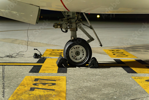 Airplane wheel on the runway waiting for takeoff, it is nighttime and the light is artificial. You can see some headsets on the ground that the coordinator uses to communicate with the pilot.