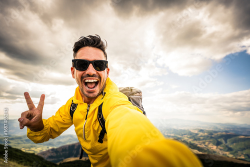 Young hiker man taking selfie portrait on the top of mountain - Happy guy smiling at camera - Hiking, sport, travel and technology concept - Bright filter