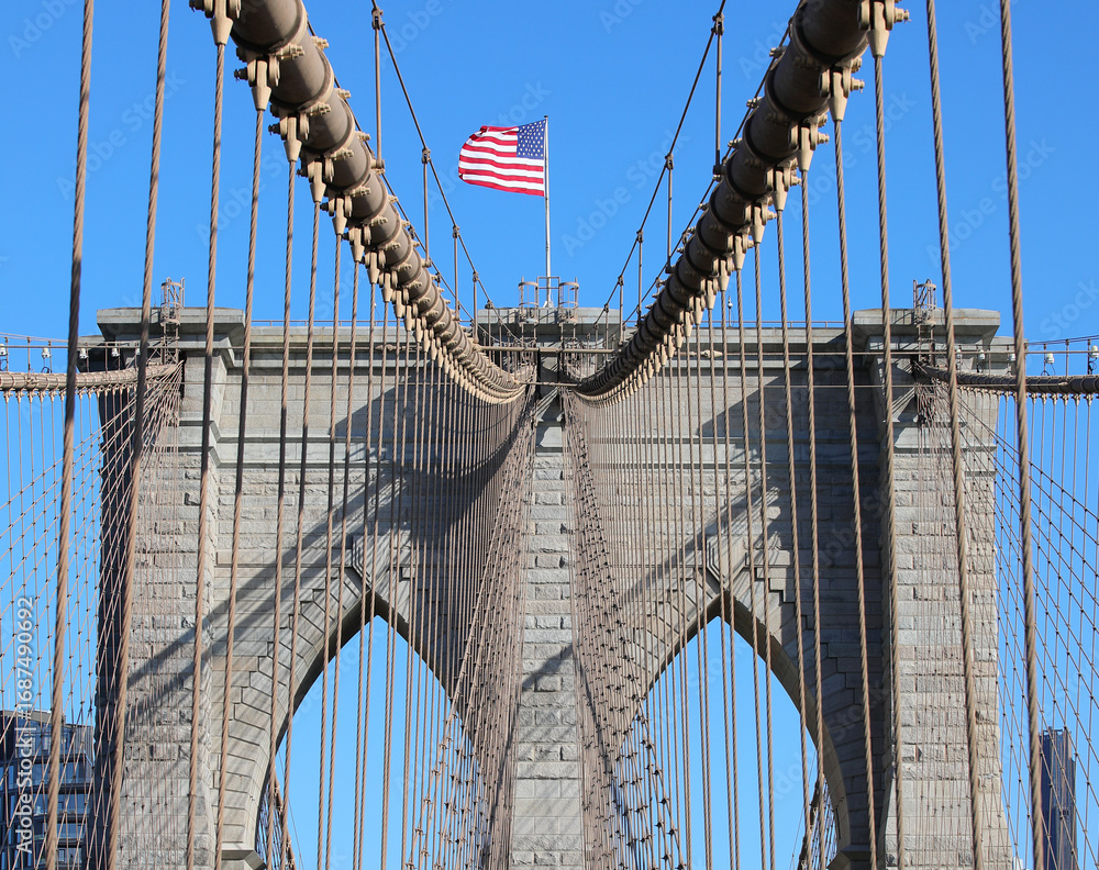 Fototapeta premium New York city with Large American Flag on the top of Tower of Brooklyn Bridge and steel cables