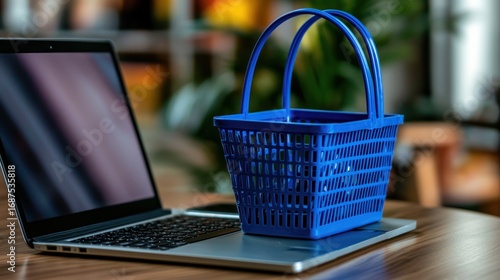 A blue shopping basket sits atop a silver laptop on a wooden surface, suggesting online shopping.