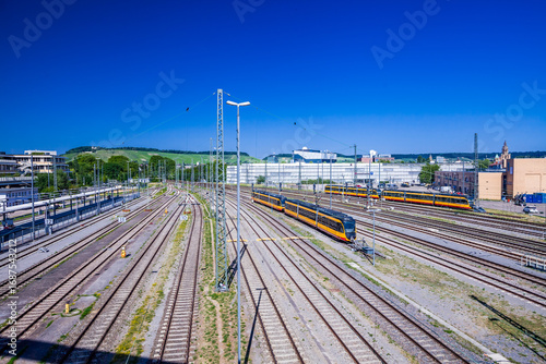From BUGA Bridge, Heilbronn station reveals both motion and stillness: side-track trains waiting under the blue noon sky.
