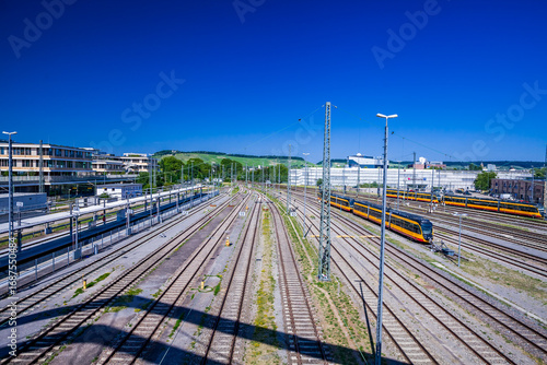 Obraz na plátně HEILBRONN, GERMANY - JUNE 21, 2025: The station’s tracks stretch into the horizon, framed by steel and sunlight, with the city’s bustle captured from BUGA Brücke