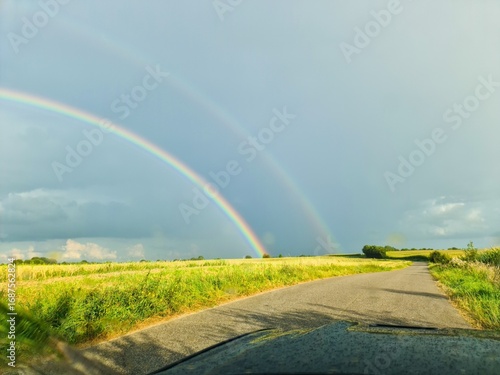 Double rainbow appearing over green field and country road after summer rain