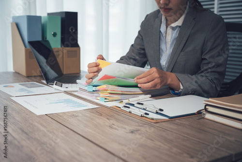 Businessman working through pile of documents to find unfinished documents, information on pile of documents on desk and checking financial documents amidst busy workload.