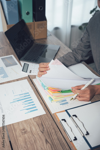 Businessman working through pile of documents to find unfinished documents, information on pile of documents on desk and checking financial documents amidst busy workload.