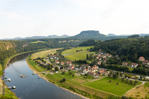 Panoramic aerial view of Saxon Switzerland National Park, Germany. Elbe river winding through green valley with a small village and Lilienstein mountain on the horizon. Scenic summer landscape in Saxo