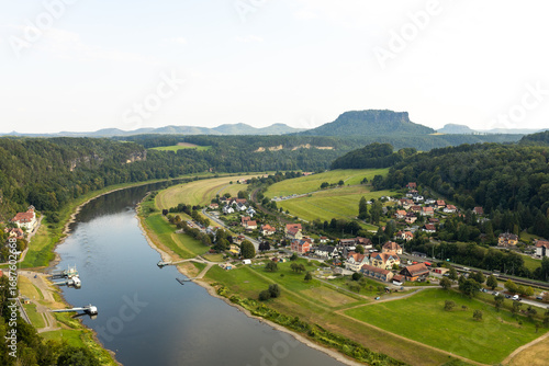 Aerial view of the Elbe River, village and green hills in Saxon Switzerland, Germany. A peaceful landscape with mountains and plains on the horizon.