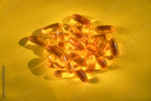 Glossy yellow softgel capsules grouped on a vibrant yellow background with natural light reflections, symbolizing vitamins, omega-3, and dietary supplements.