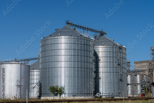 Storage silos support grain operations in a large agricultural warehouse under clear blue sky
