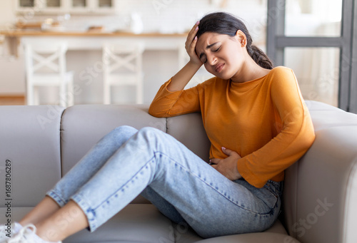 Fototapet Sad young indian woman suffering from PMS and menstruation pain at home, upset e