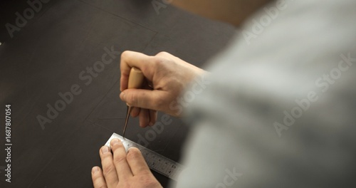 Fotografie Craftsman using awl and ruler to mark layout lines on leather surface during han
